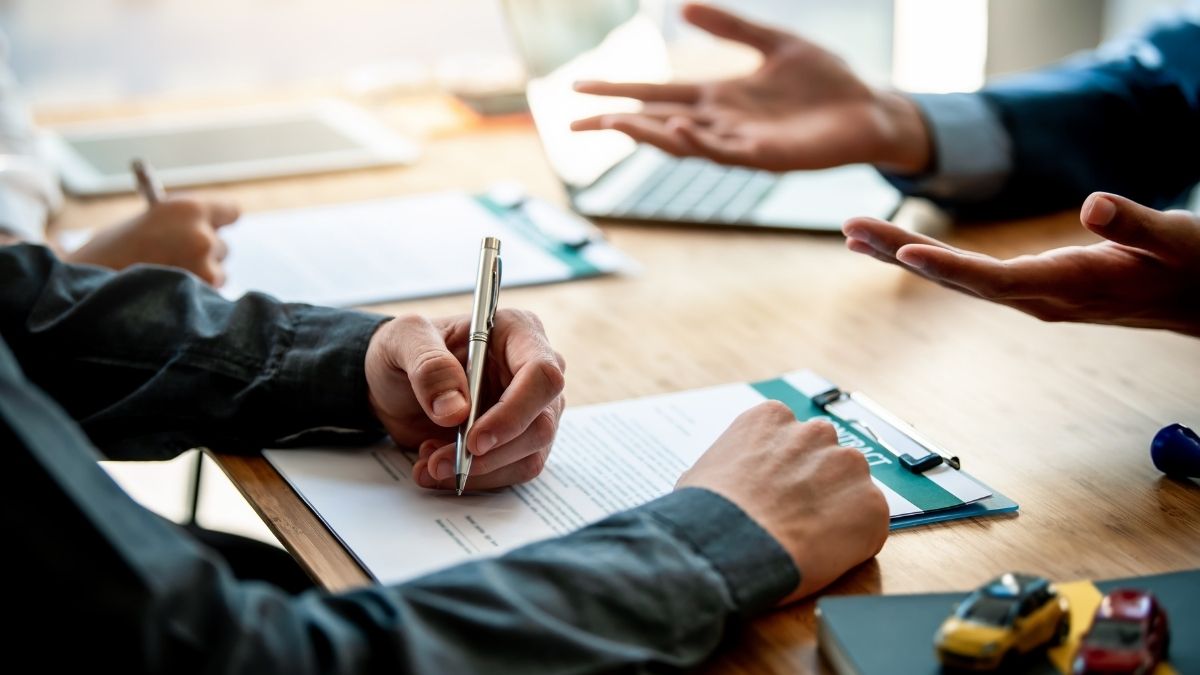 Close-up of a business meeting with three people discussing documents on a wooden table. Hands gesture dynamically, suggesting a lively conversation.